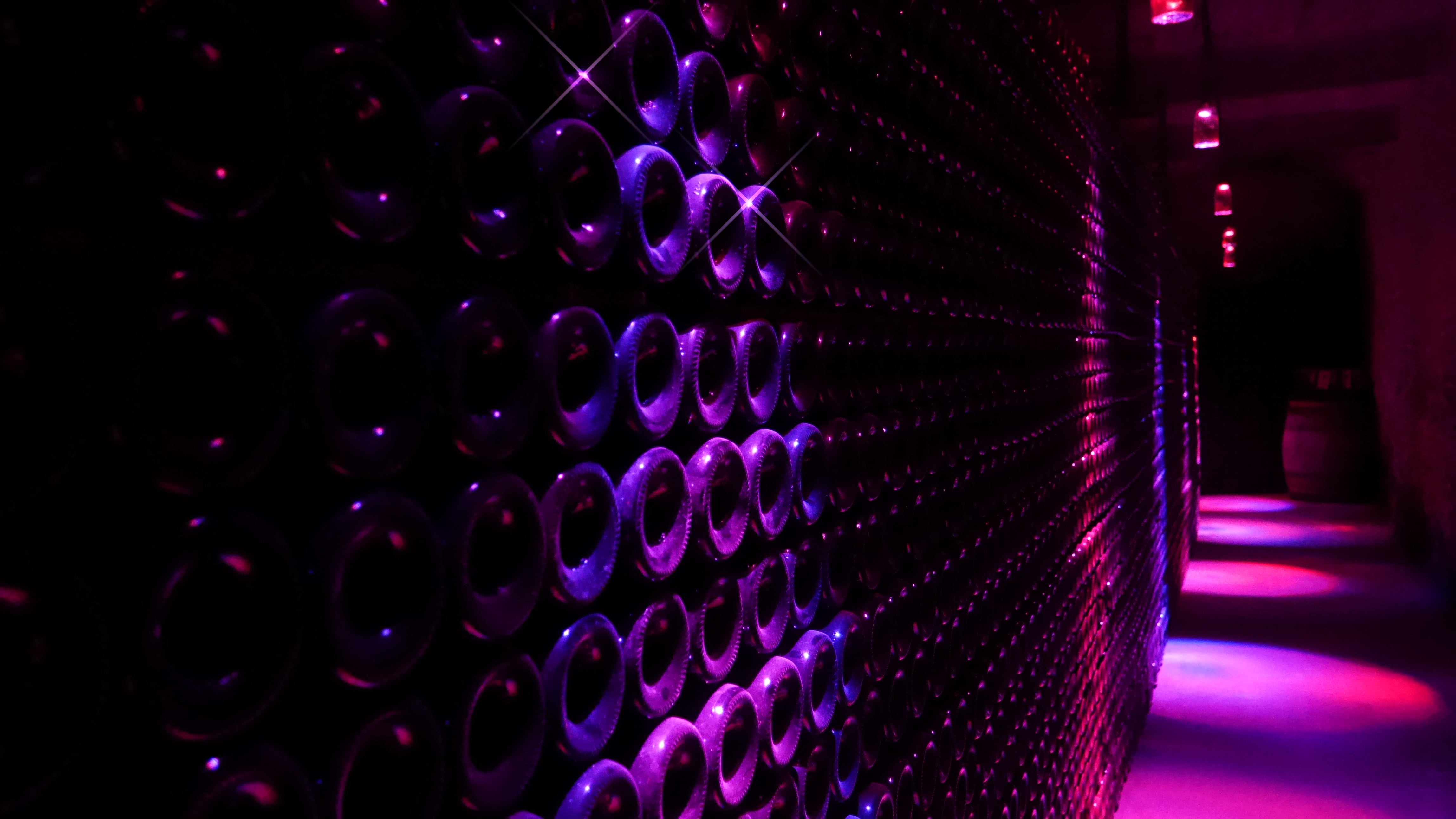 Bouteilles en vieillissement dans les caves Bulles & Lumières de la Maison Guinot, éclairées en violet et rose.
